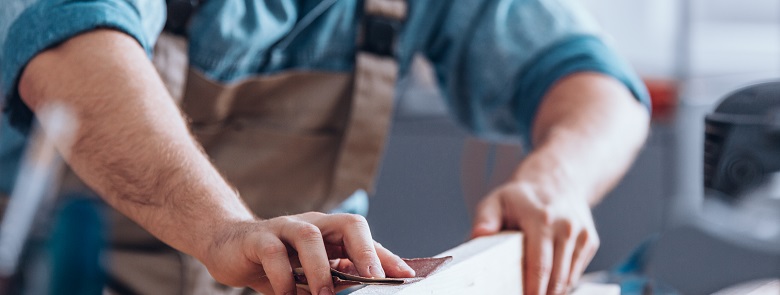 Close-up of male carpenter using sandpaper on a piece of wood for furniture