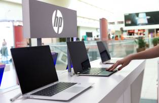Bancada com diversos notebooks da HP, com o logo da companhia atrás