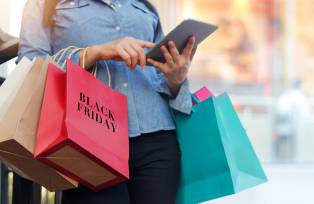 Mulher segurando tablet enquanto carrega sacolas da Black Friday