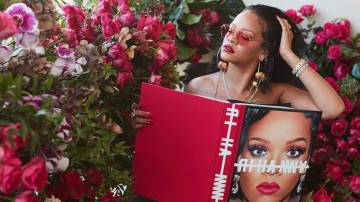 Cantora Rhianna posa sentada com um livro vermelho sob seu colo ao lado de muitas rosas