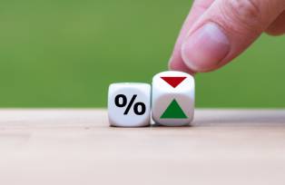 Hand is turning a dice and changes the direction of an arrow symbolizing that the interest rates are going down (or vice versa)