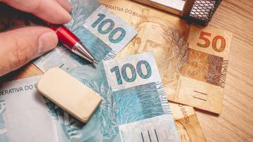 Real - Brazilian Currency. Money bills on a wooden table and a man holding a pen.