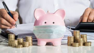 Businessman Calculating Invoice With Piggybank And Coins At Desk