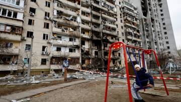 Criança sentada em balanço na frente de um prédio residencial destruído após a Rússia lançar operação militar contra a Ucrânia, em Kiev, 25 de fevereiro de 2022