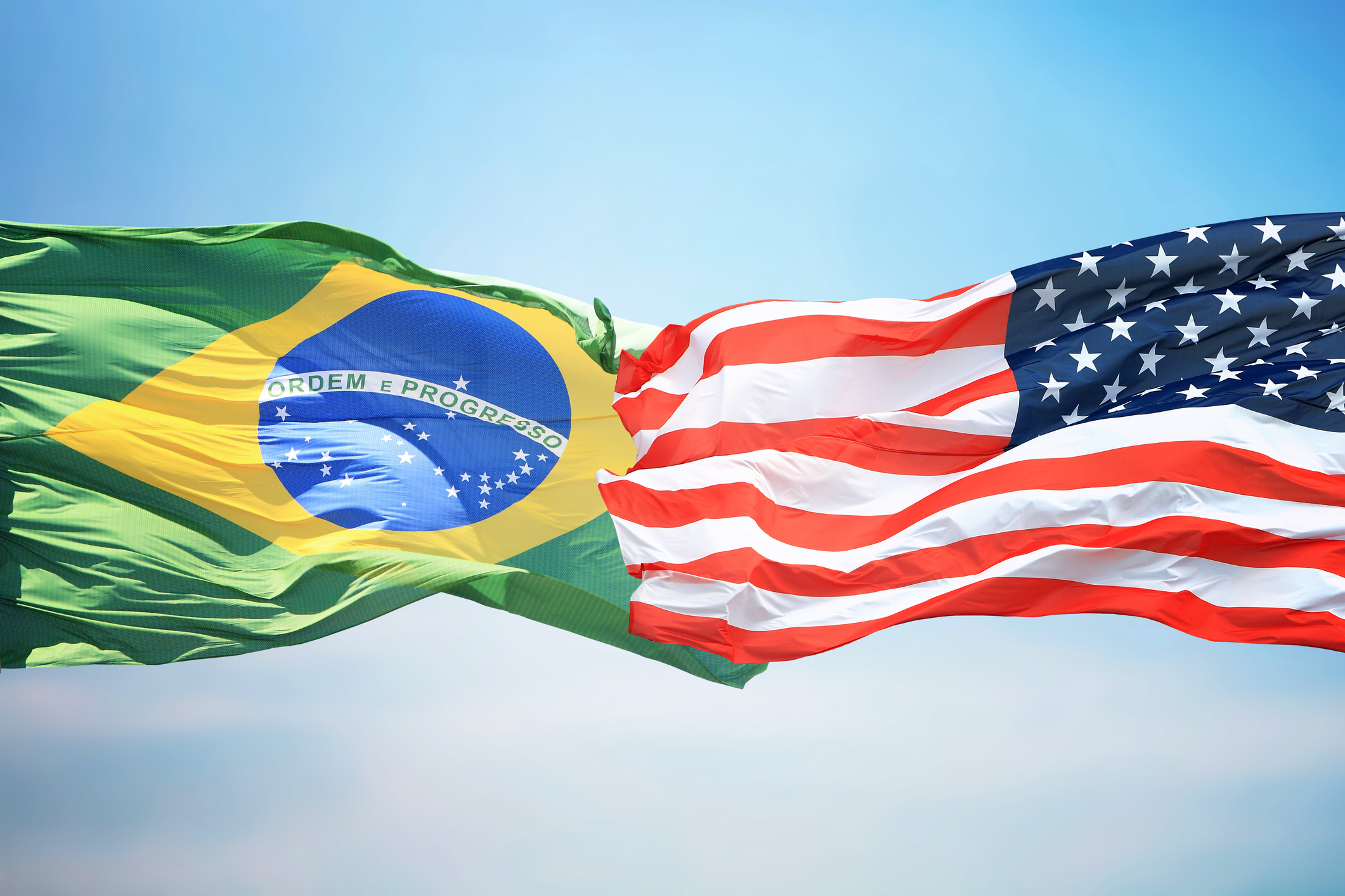 Flag of the USA and Brazil against the background of the blue sky