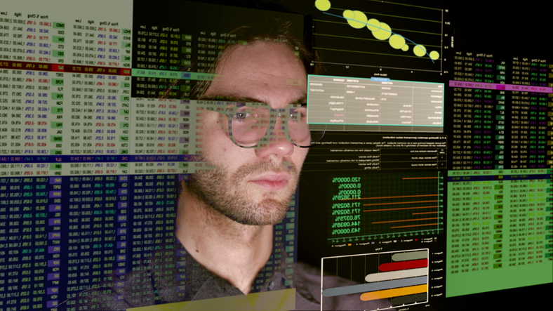 Close up stock image showing a young bearded man analysing numbers, financial figures on a large see-thru (see through) computer display.