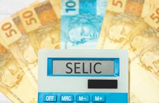 Foto de stock de As iniciais SELIC referem-se à taxa básica de juros no Brasil escritas na exibição de uma calculadora com notas de reais na composição. Economia e investimentos brasileiros.