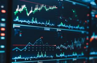 Foto de stock de Close Up Shot de uma tela de monitor de computador com ações em tempo real, commodities e gráficos de mercado de câmbio e tickers em uma estação de trabalho multi-display em um Escritório de Negócios Financeiros.