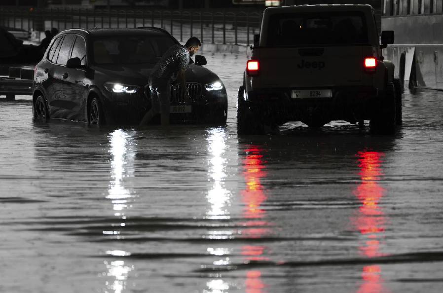 Um homem tenta trabalhar em seu SUV parado em águas paradas em Dubai, Emirados Árabes Unidos, terça-feira, 16 de abril de 2024. (AP Photo/Jon Gambrell)