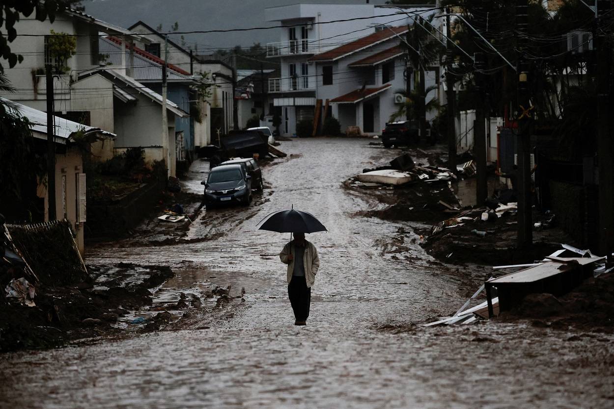 Homem com guarda-chuva caminha por uma rua parcialmente destruída após enchentes em Muçum, no Rio Grande do Sul (Foto: Adriano Machado/Reuters)