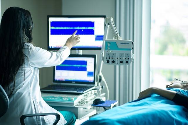 Médica mexendo em tela de equipamento médico ao lado de um paciente