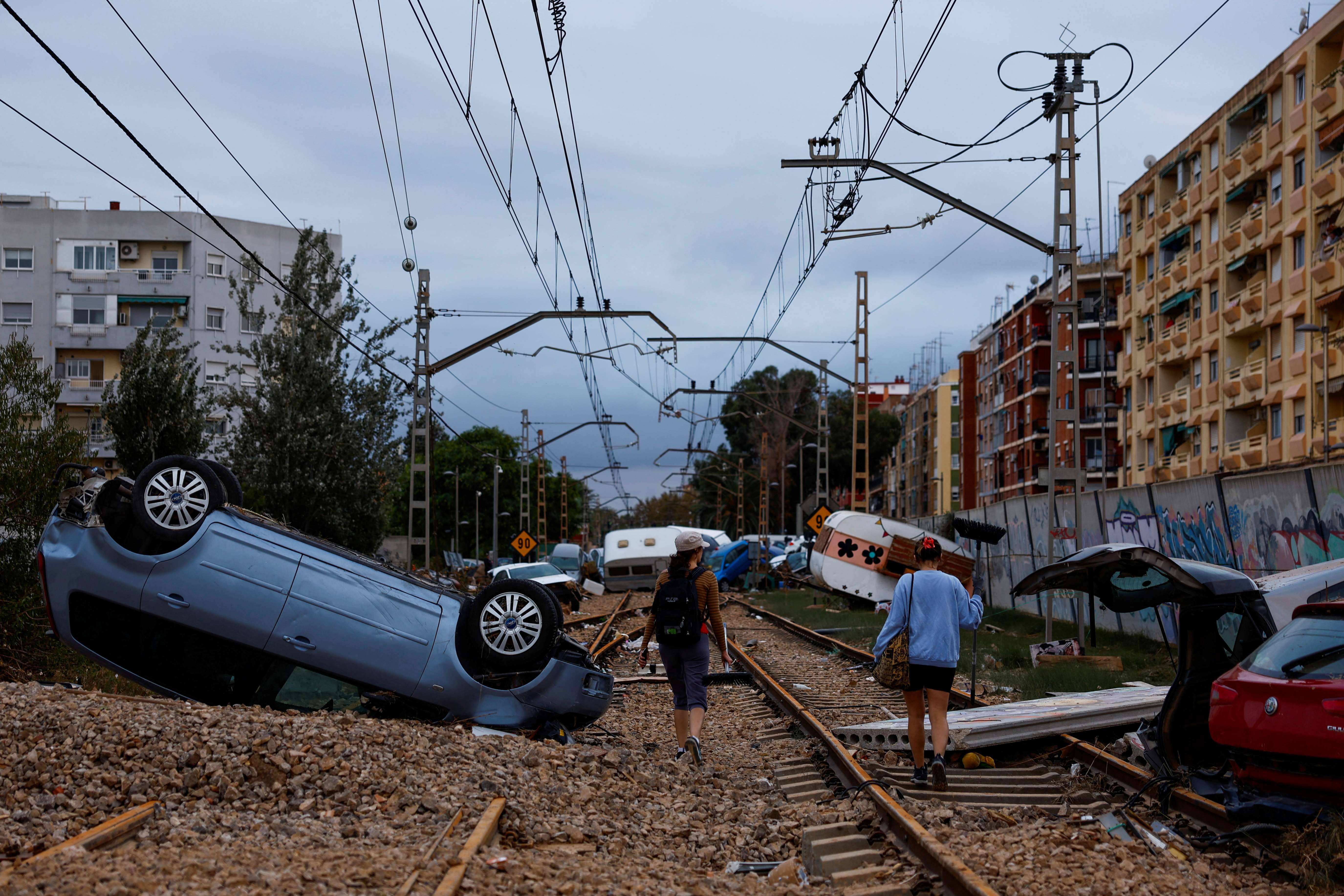 Mulheres caminham ao lado carros tombados ao longo dos trilhos da ferrovia, em Alfafar, Espanha, - 31/10/2024 (Foto: Susana Vera/Reuters)