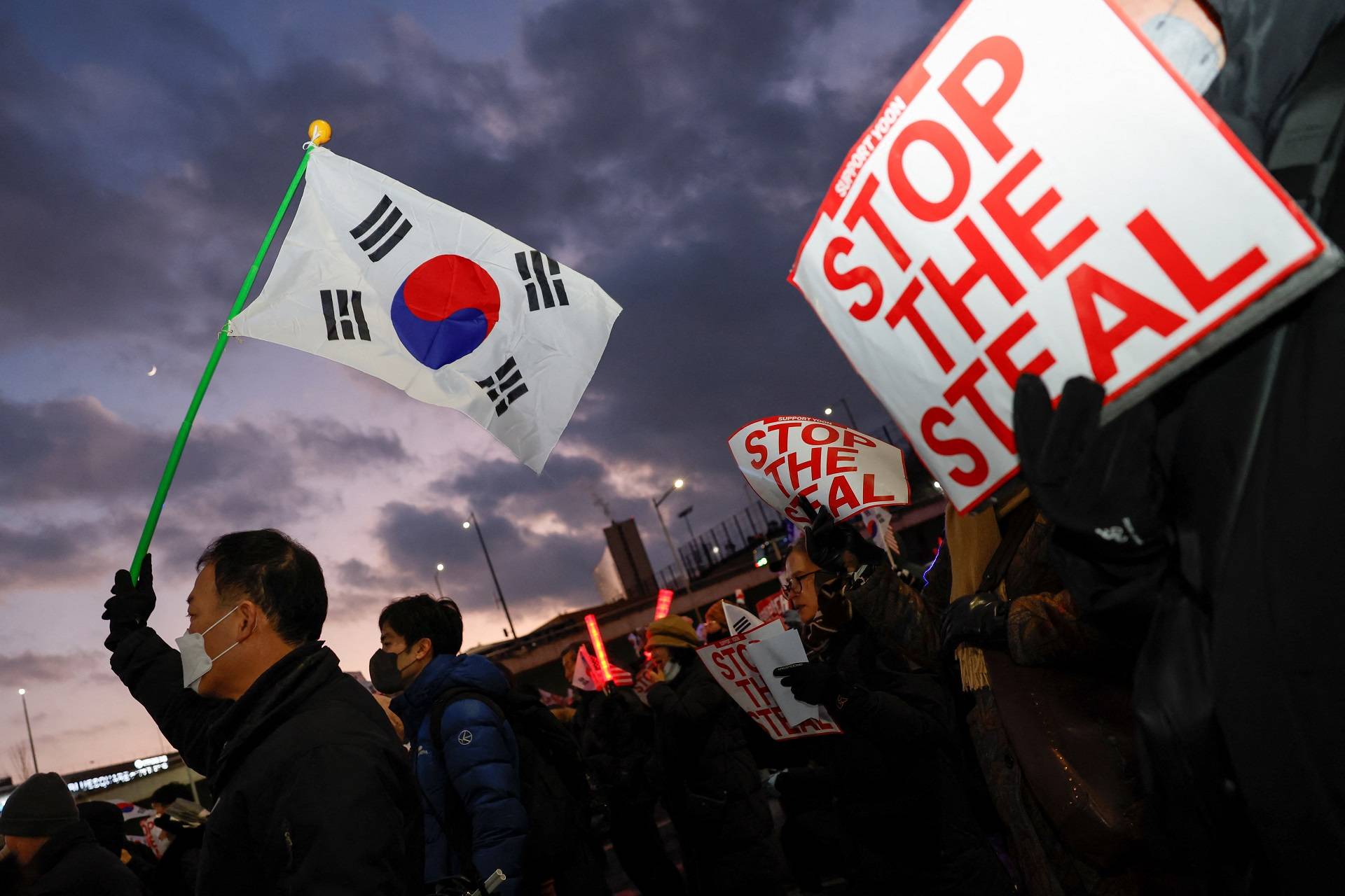 Manifestantes pró-Yoon seguram bandeiras sul-coreanas e cartazes com os dizeres "PAREM O ROUBO" durante um protesto perto da residência oficial do presidente sul-coreano Yoon Suk Yeol, após os investigadores não conseguirem executar um mandado de prisão na sexta-feira para Yeol, de acordo com o Escritório de Investigação de Corrupção para Altos Funcionários, em Seul, Coreia do Sul, 3 de janeiro de 2025. REUTERS/Kim Soo-hyeon