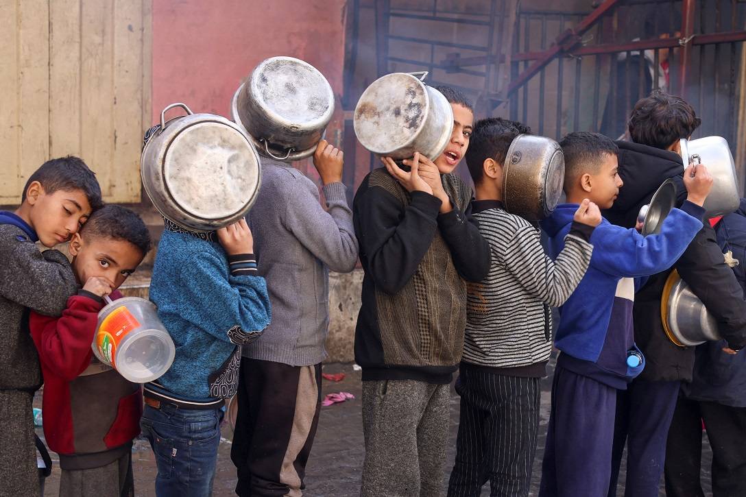 Crianças palestinas carregam panelas enquanto fazem fila para receber comida preparada por uma cozinha de caridade, em Rafah, no sul da Faixa de Gaza
24/12/2023
REUTERS/Saleh Salem