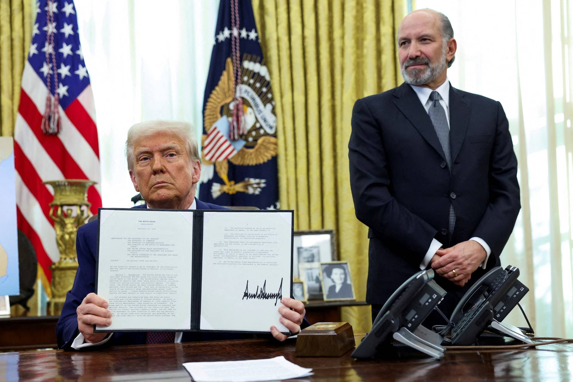 O presidente dos EUA, Donald Trump, segura uma ordem executiva sobre o aumento de tarifas, ladeado pelo secretário de Comércio dos EUA, Howard Lutnick, no Salão Oval da Casa Branca em Washington, D.C., EUA, 13 de fevereiro de 2025. REUTERS/Kevin Lamarque