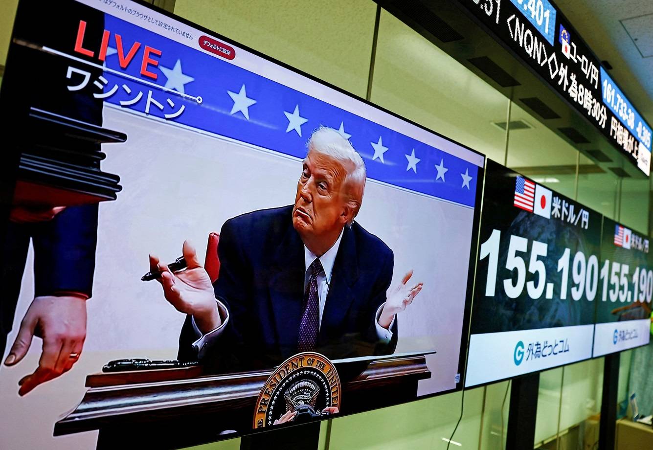 Uma tela transmitindo imagens ao vivo no Japão mostra o presidente dos EUA, Donald Trump, gesticulando enquanto assina ordens executivas - 21/01/2025 (Foto:  REUTERS/Issei Kato)