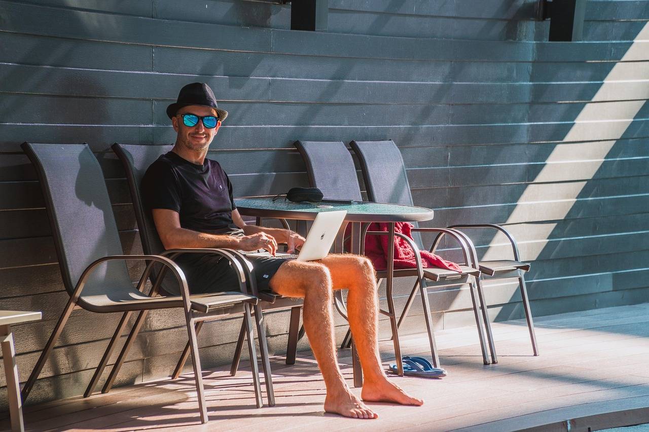 Homem trabalha com computador em beira de piscina