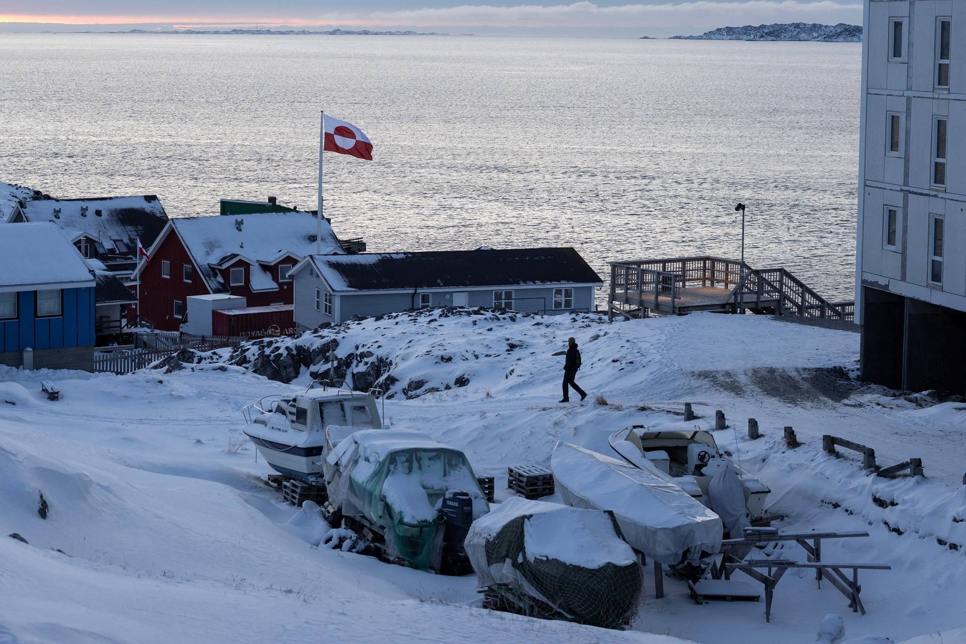 Uma bandeira da Groenlândia tremula enquanto um homem caminha no dia do encontro entre altos funcionários dos EUA e os ministros das Relações Exteriores da Dinamarca e da Groenlândia, em Nuuk, Groenlândia, 14 de janeiro de 2026. REUTERS/Marko Djurica