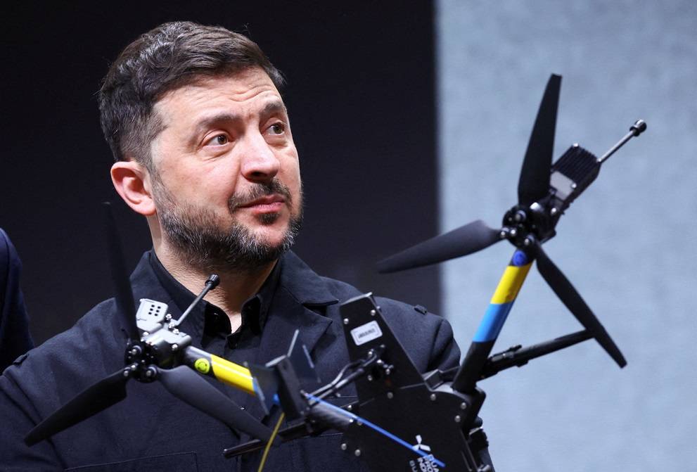 O presidente da Ucrânia, Volodymyr Zelenskiy, reage ao ser fotografado atrás de um drone durante visita a uma instalação da fabricante alemã de drones Quantum Systems, à margem da Conferência de Segurança de Munique (MSC), perto de Munique, Alemanha, em 13 de fevereiro de 2026. REUTERS/Thilo Schmuelgen TPX IMAGES OF THE DAY

