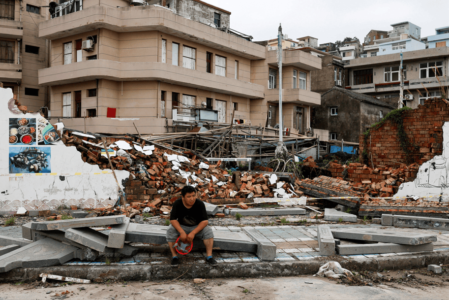 Uma pessoa senta-se ao lado de um muro desmoronado após a passagem do tufão Bavi na vila costeira de Dongsha, em Taizhou, província de Zhejiang, China, 12 de julho de 2026